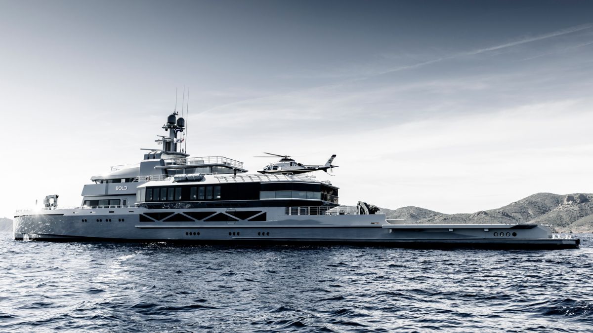 A large luxury yacht anchored on calm waters, featuring multiple decks, a helicopter on the helipad, and mountain silhouettes in the background, all captured in a monochrome tone.