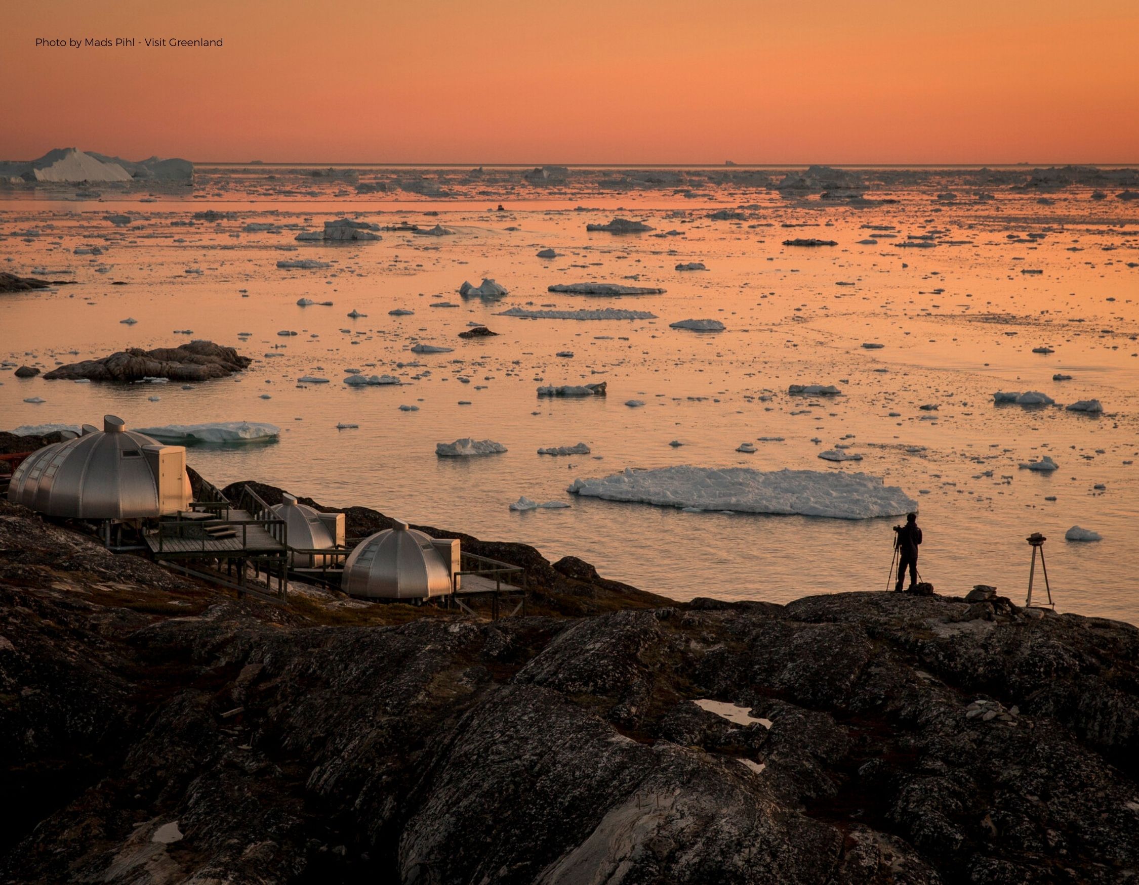 Man with camera overlooking icy sea under orange Arctic sky – Pelorus Yachting 2026 Greenland solar eclipse expedition.