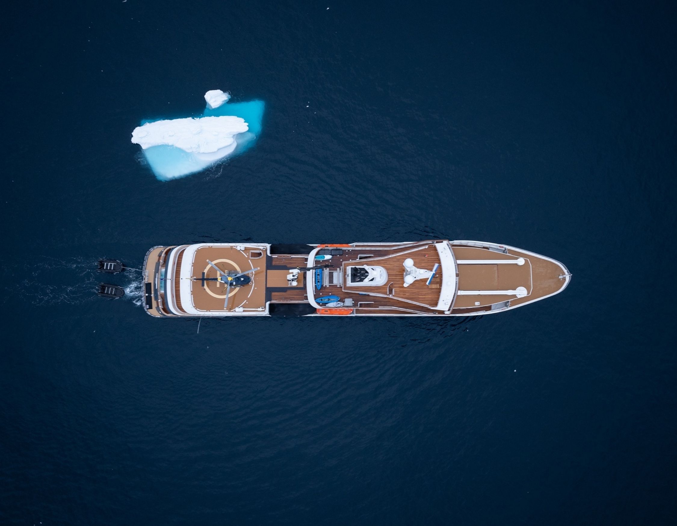 Aerial view of superyacht AQUA LARES navigating icy Greenland waters alongside iceberg. Pelorus Yachting 2026 Luxury Greenland Arctic voyage