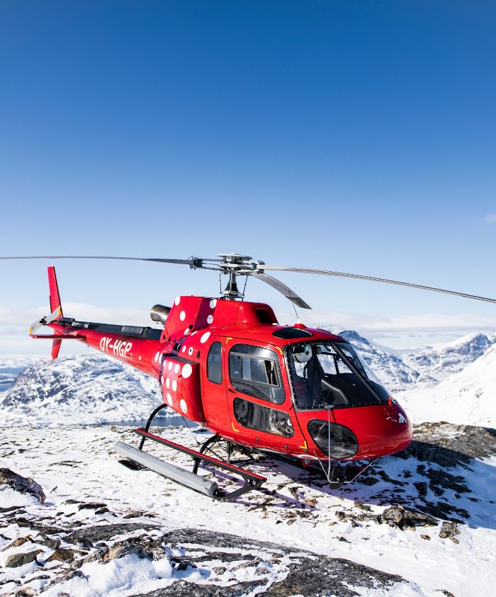 Red helicopter atop a glacier for a luxury yacht charter in Greenland