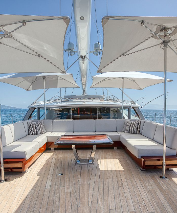 Flybridge of large luxury sailing yacht with sofas and outdoor al fresco dining area and umbrellas overlooking the blue sea