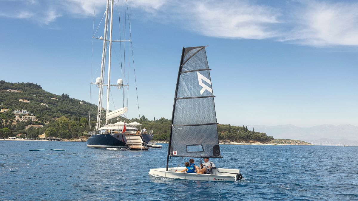 Large luxury sailing yacht in the blue sea infront of cliffs with tress and a small sailing boat crossing behind