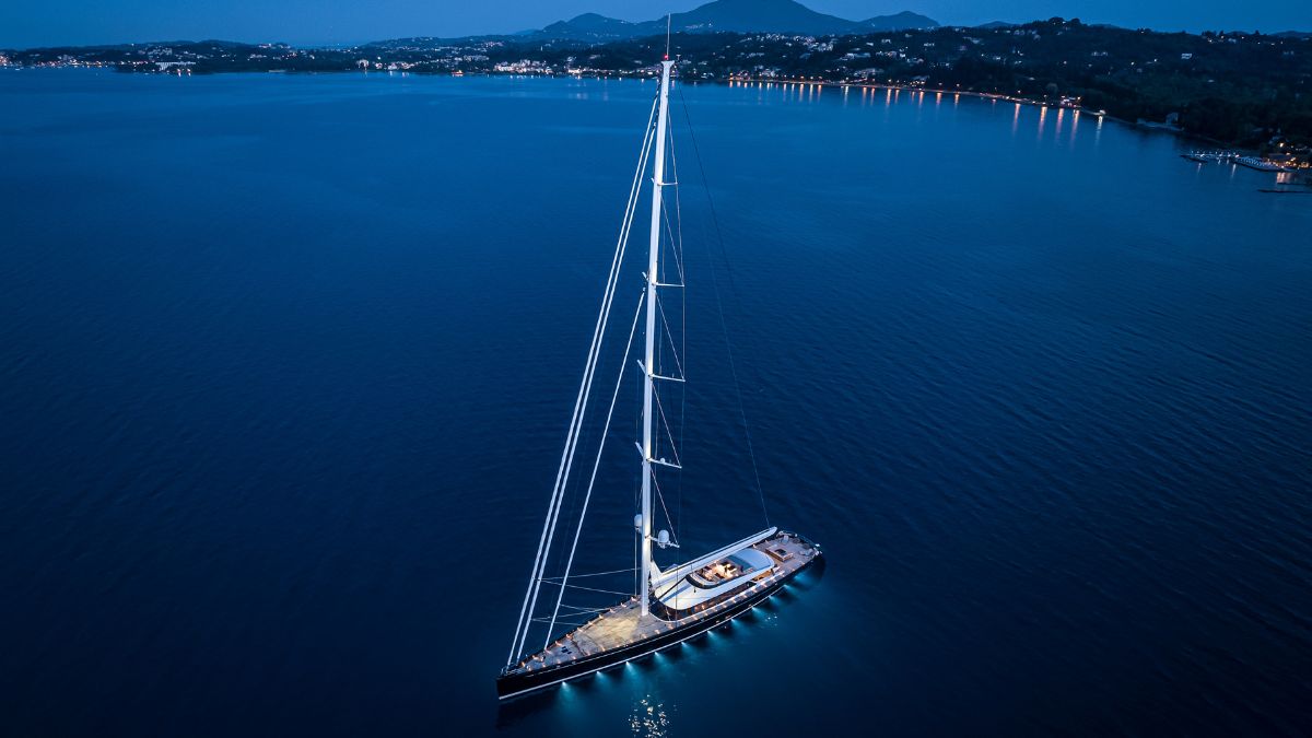 Large luxury sailing yacht at night time with mast and underwater lights. Sat in the deep blue ocean overlooking the bay.