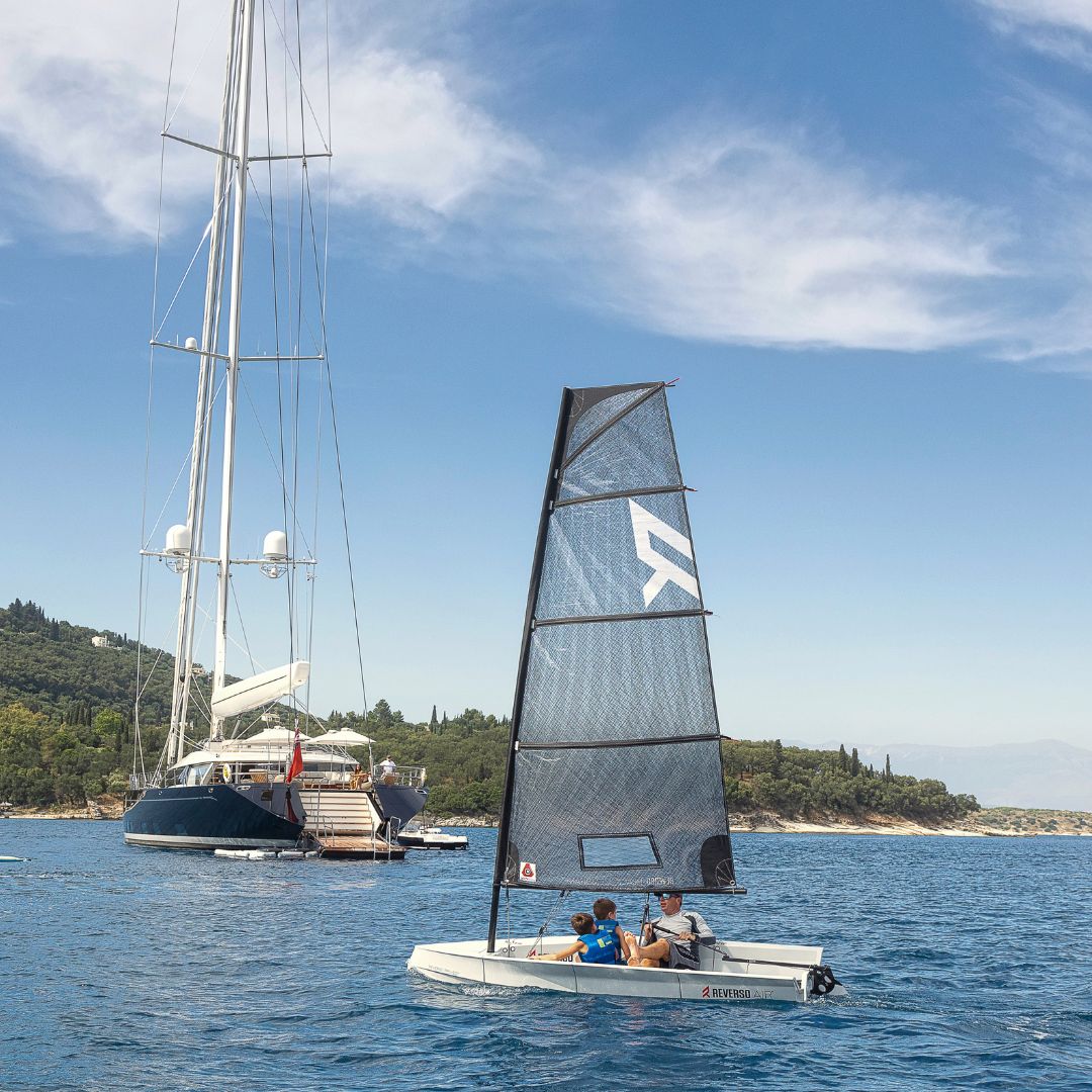 Back of large luxury sailing yacht in blue sea with trees in the background and a small sailing boat crossing behind