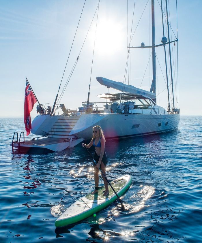 Luxury sailing yacht with national flag and woman paddleboarding – Pelorus Yachting 2026 luxury yacht charter Odyssey adventure.
