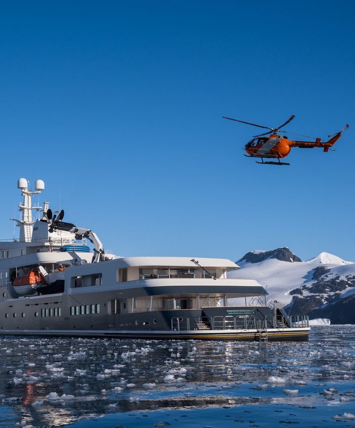 Luxury superyacht charter AQUA LARES with helicopter landing in icy Greenland waters under solar eclipse – Pelorus Yachting 2026 Arctic expedition.