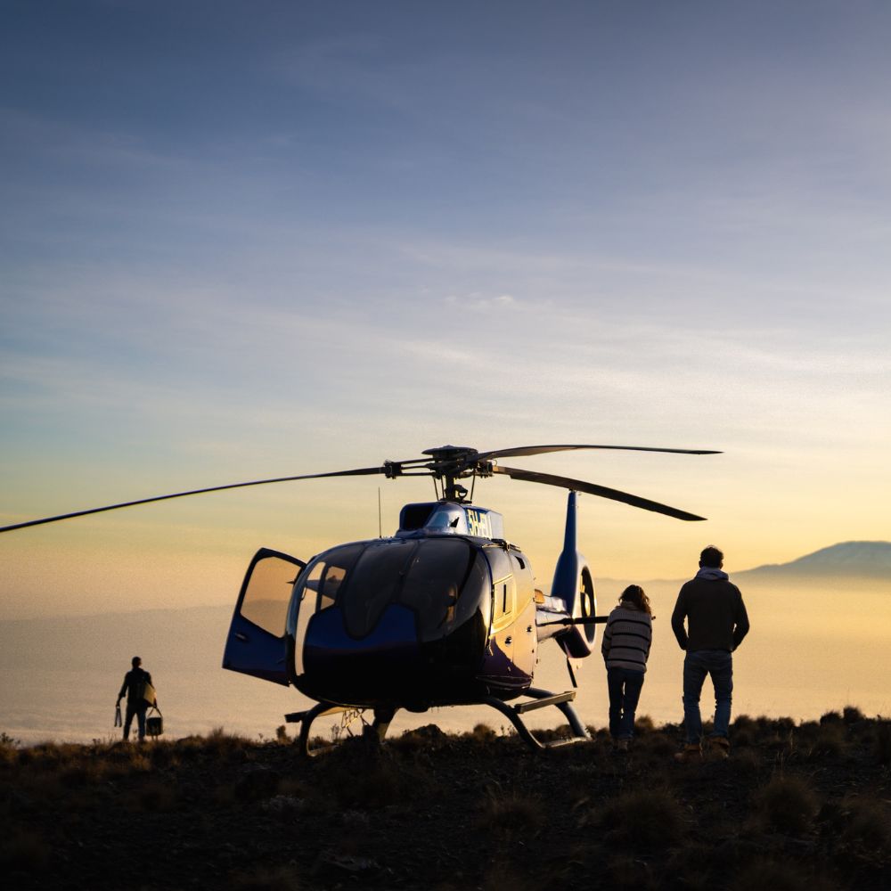 People stood by a helicopter looking at the sunrise in Tanzania